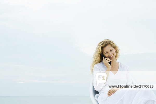 Frau sitzt im Sessel im Freien  telefoniert mit dem Handy  lächelt