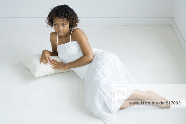 Junge Frau auf Kissen auf dem Boden liegend  wegschauend  volle Länge