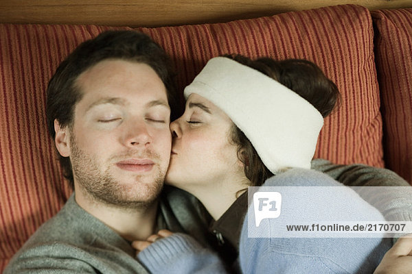 Junges Paar auf Couch liegend  Frau küssend Mann auf Wange  Augen geschlossen