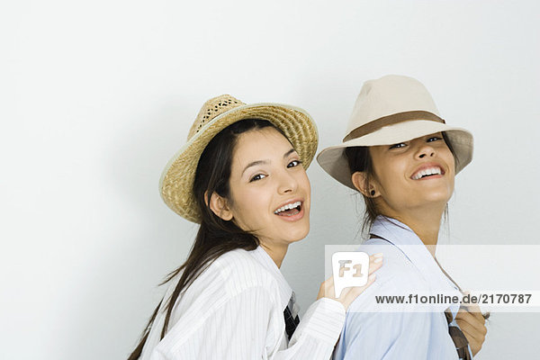 Two young female friends wearing hats and ties  smiling at camera  one placing hand on the other's shoulder