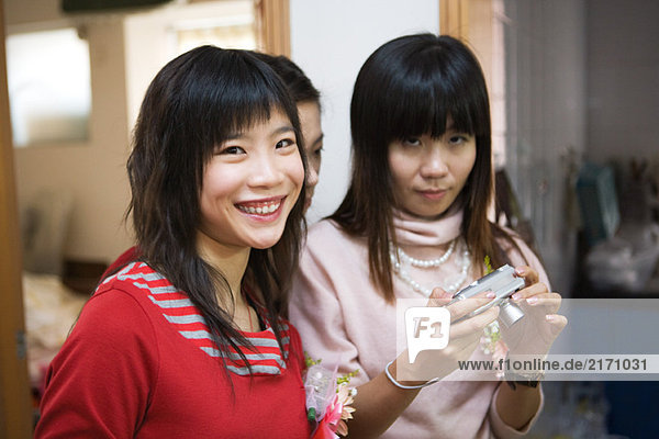 Three young women wearing corsages  one holding digital camera
