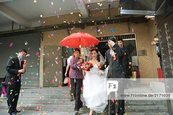 Chinese wedding  bride and groom leaving under confetti  bride covered by red parasol