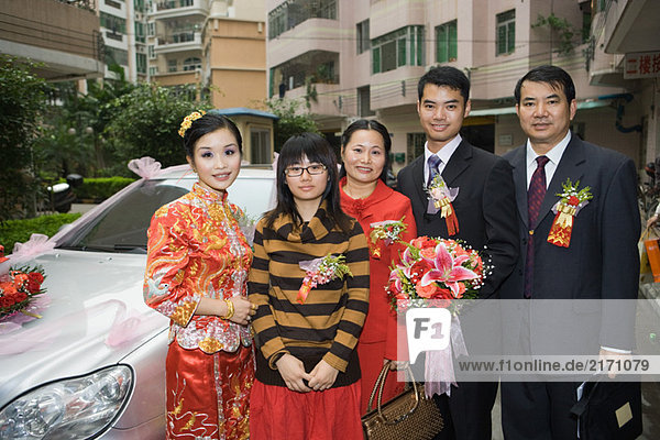 Bride and groom standing with parents and sister in front of car  portrait