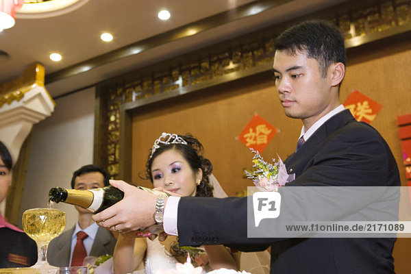 Braut und Bräutigam gießen gemeinsam Champagner an der Rezeption.
