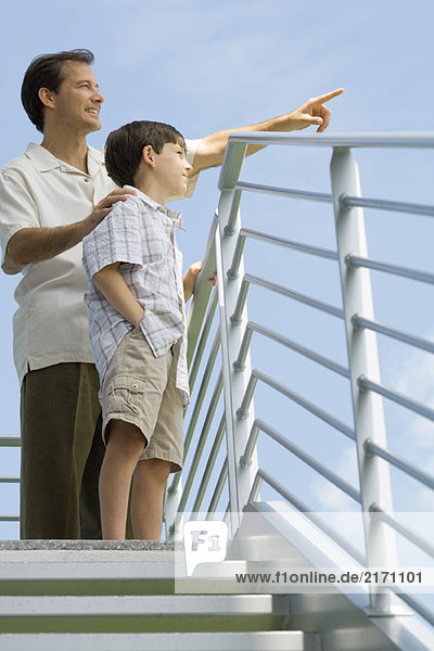 Man standing at top of staircase with son and pointing at sky  low angle view