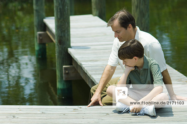 Vater und Sohn sitzen auf dem Dock und schauen gemeinsam nach unten.