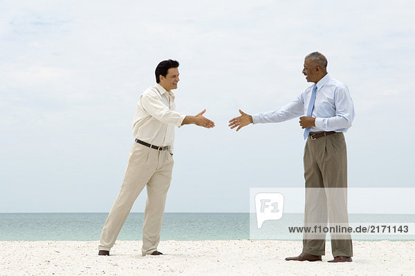 Zwei Geschäftsleute  die am Strand stehen und sich gegenseitig die Hände schütteln.