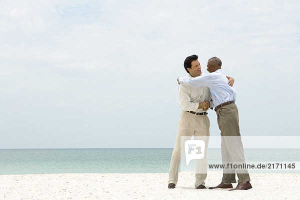 Zwei Geschäftsleute schütteln sich die Hand und umarmen sich am Strand.