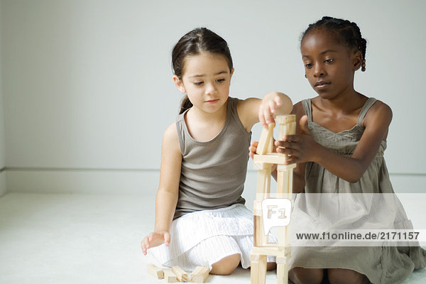 Zwei Mädchen hocken  bauen Turm mit Blöcken zusammen