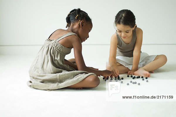 Zwei Mädchen sitzen auf dem Boden und spielen mit Murmeln.