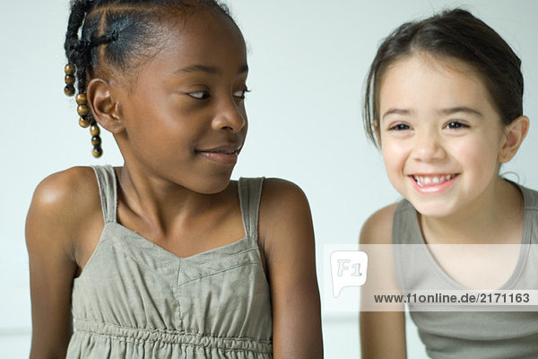Zwei Mädchen lächeln Seite an Seite  eine schaut die andere an.