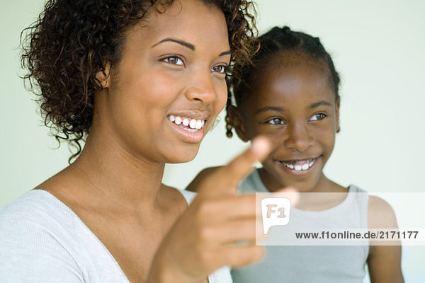 Young woman pointing finger and looking away with daughter  both smiling