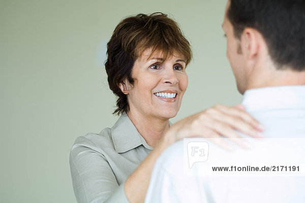 Senior woman standing in front of adult son with her hand on his shoulder  smiling