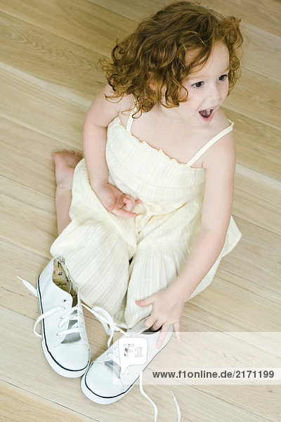 Kleines Mädchen kniend auf dem Boden in der Nähe von Schuhen  überrascht aussehend