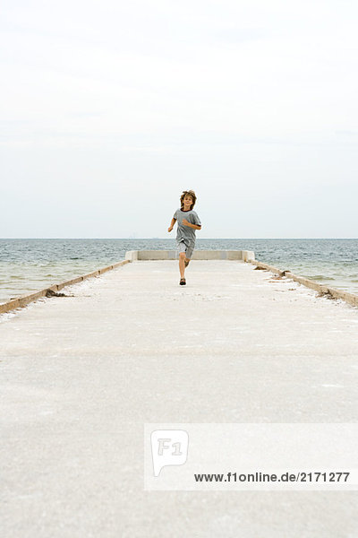 Boy running on pier  towards camera  ocean in background