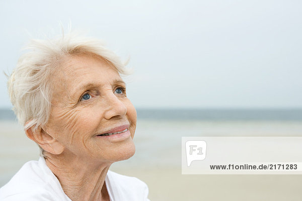 Seniorin lächelnd  aufblickend  Strand im Hintergrund