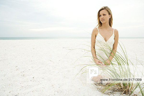 Frau kniend am Strand bei Dünengras  wegschauend  volle Länge