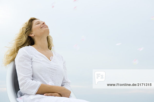 Frau sitzend mit geschlossenen Augen und Kopf zurück  lächelnd  Himmel im Hintergrund  Tiefblick