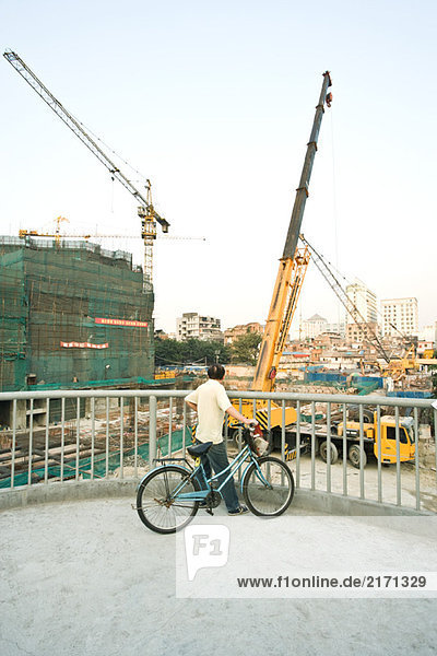 Mann mit Fahrrad auf der Baustelle  Rückansicht