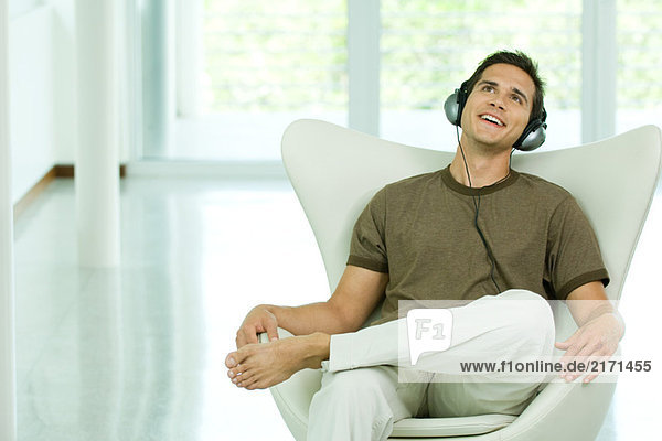 Young man sitting in chair listening to headphones  smiling