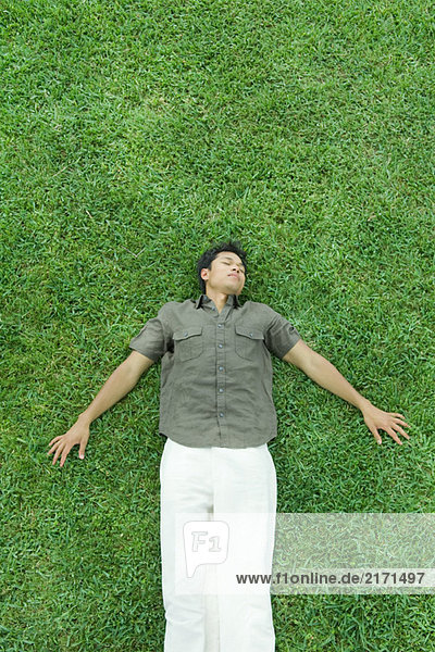 Mann auf dem Rücken im Gras liegend  Augen geschlossen  volle Länge