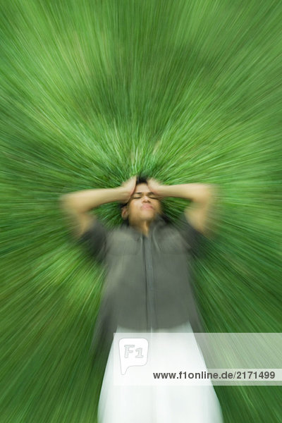 Mann auf dem Rücken liegend im Gras mit geschlossenen Augen  Kopf haltend  verschwommene Bewegung