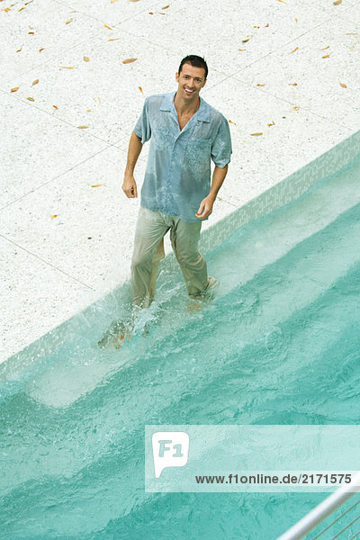 Mann beim Plantschen im Pool  voll bekleidet  lächelnd vor der Kamera  hoher Blickwinkel