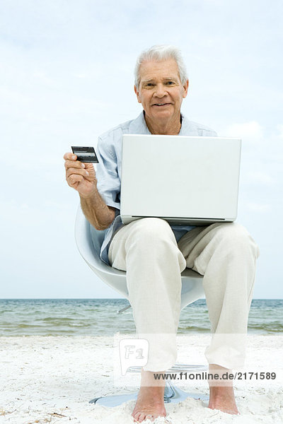 Senior Mann mit Laptop am Strand  die Online-Einkauf mit Kreditkarte