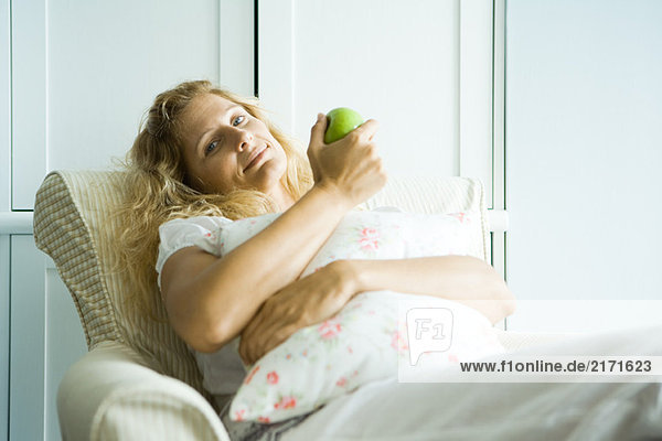 Frau im Sessel sitzend  Apfel haltend  lächelnd vor der Kamera