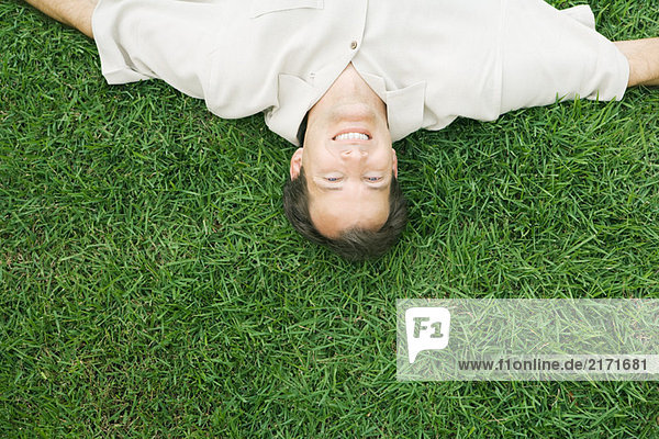 Man lying upside down in grass  smiling at camera  cropped high angle view