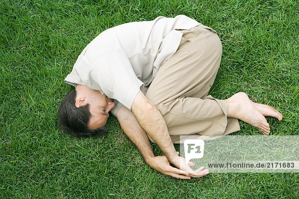 Mann in fetaler Position auf Gras liegend  Augen geschlossen  Hochwinkelansicht