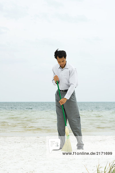 Mann am Strand stehend mit Besen  volle Länge