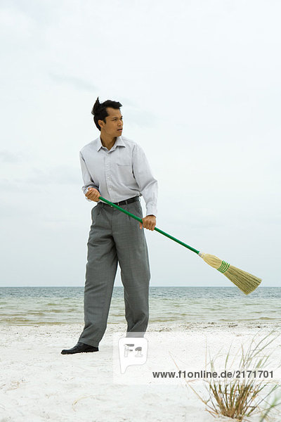 Mann am Strand stehend  mit Besen fegend  wegschauend