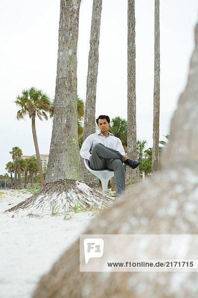 Mann im Stuhl am Strand sitzend  mit Blick auf die Kamera  Blick in den niedrigen Winkel
