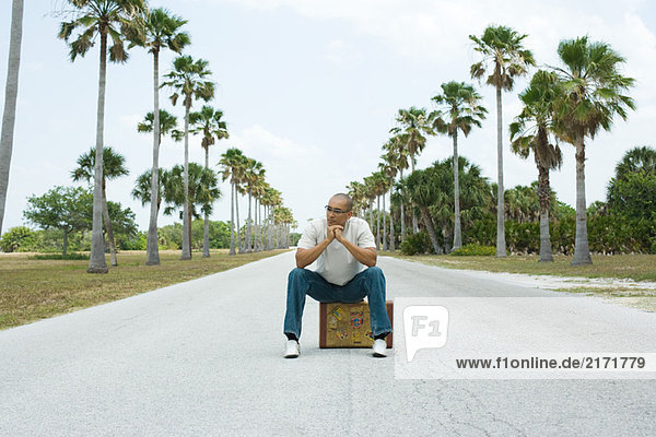 Man sitting on suitcase in the middle of street  looking away