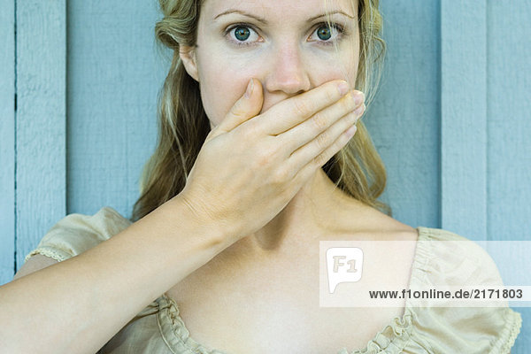 Woman covering mouth with hand  looking at camera with wide eyes
