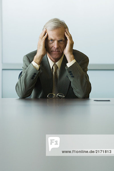Businessman sitting with head in hands  looking at camera