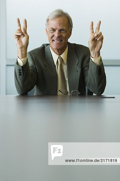 Businessman making peace signs with both hands  smiling at camera