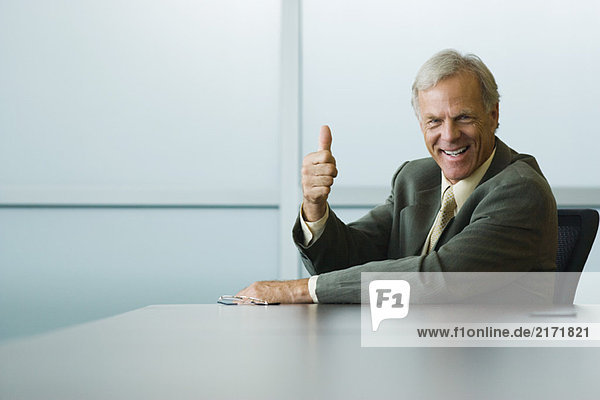 Businessman making thumbs up gesture and smiling at camera