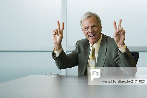 Businessman making peace signs with both hands  smiling at camera