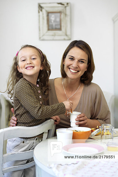 Portrait of girl and her mother smiling at breakfast table