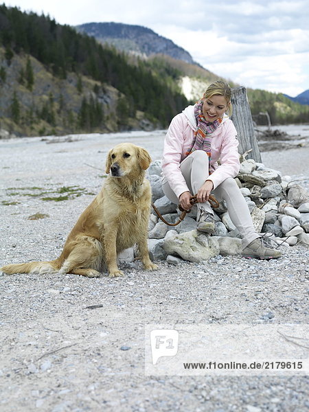 Junge Frau sitzend mit Hund am Flussufer