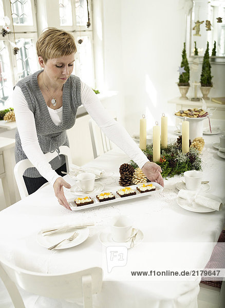 Woman placing tray of cakes on dining table