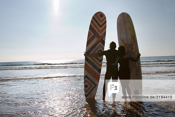 Paar mit Surfbrettern am Strand.