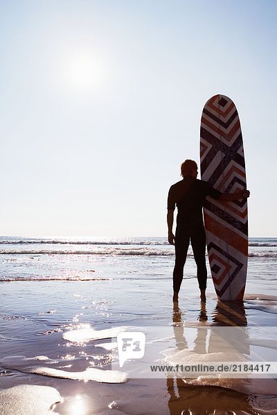 Man standing on beach with surfboard.