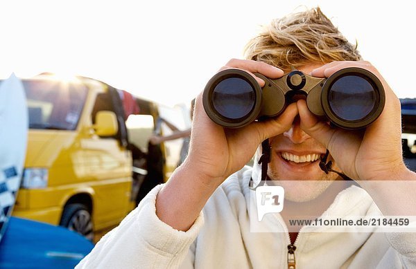 Man on beach with binoculars smiling with woman unloading van at the beach .