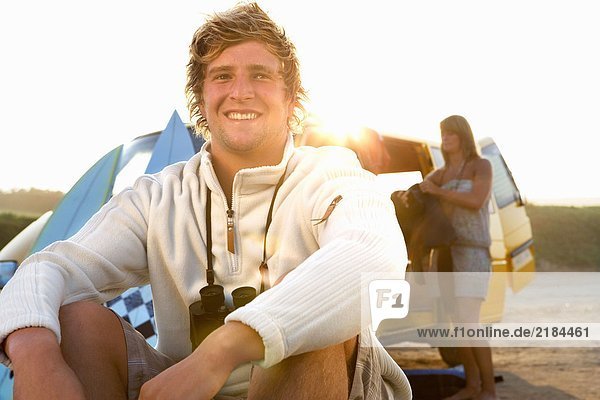Mann am Strand sitzend lächelnd mit Frau beim Entladen des Lieferwagens am Strand .