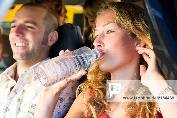 Vier Leute in einem Van lächeln mit einer Frau  die Wasser trinkt.