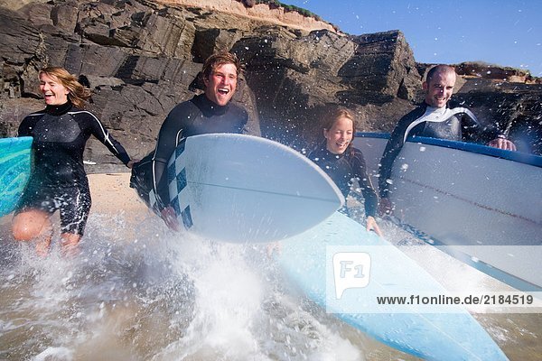 Vier Leute laufen mit lächelnden Surfbrettern ins Wasser.