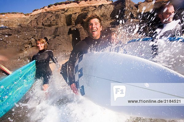 Vier Leute laufen mit lächelnden Surfbrettern ins Wasser.
